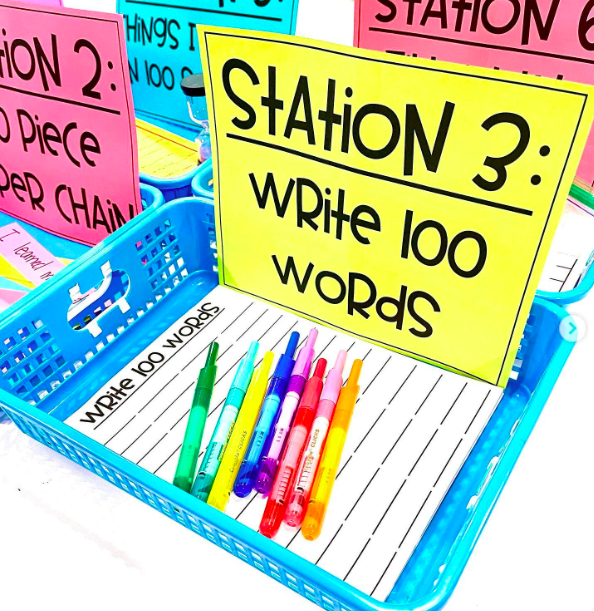 A colorful bin with the label: "Station 3 Write 100 Words" holds writing paper and colored pens 