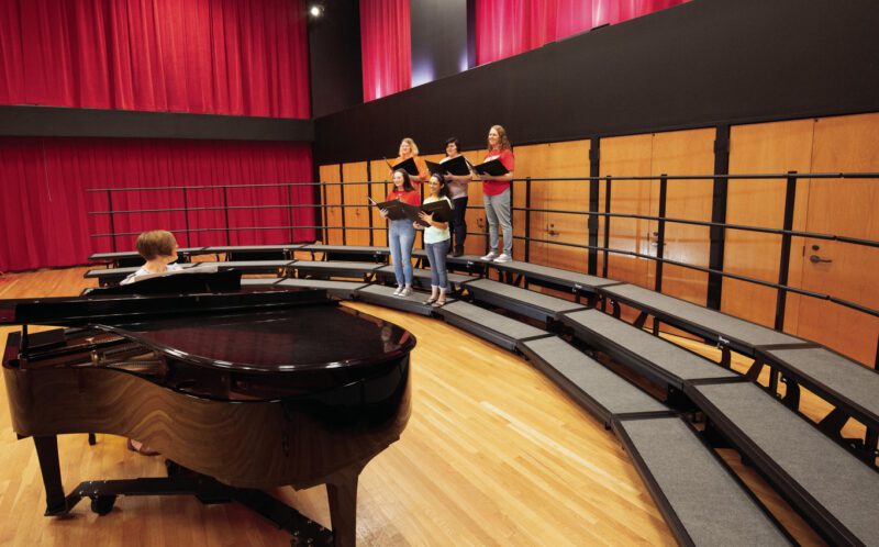 School auditorium with teacher playing grand piano and five singing high school students students standing on Wenger Signature Choral Risers
