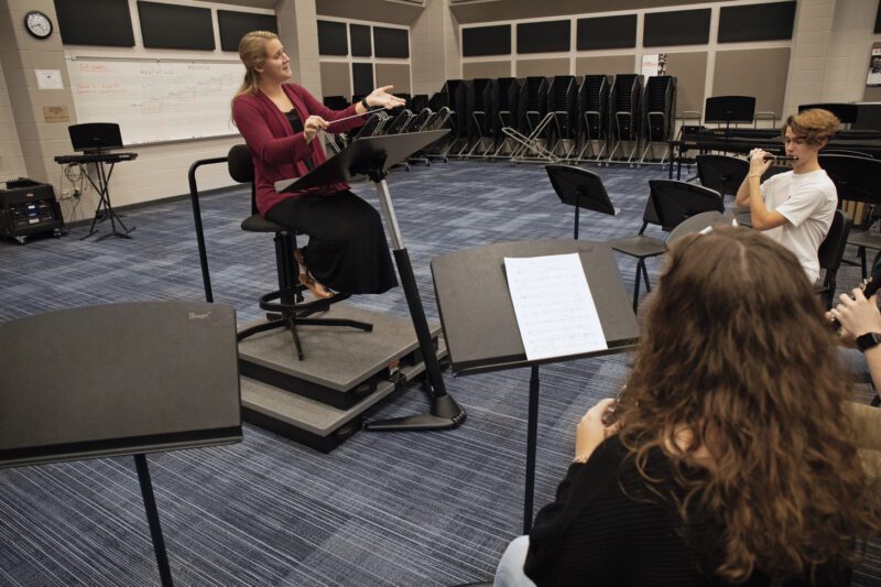 Woman conductor seated on Conductor's System and directing students in classroom