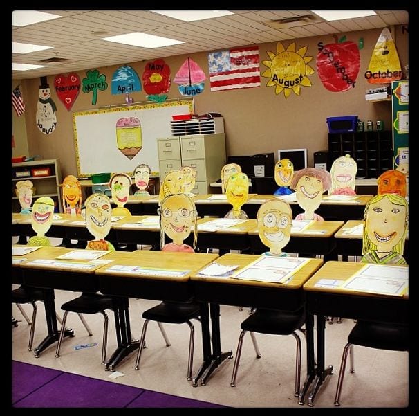rows of desks in a classroom with student made self portraits propped up on each desk as an back-to-school night idea when teaching 3rd grade
