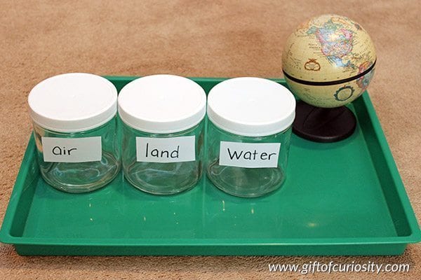 green tray with three glasses labeled air, land and water plus a tiny globe, as an example of tips for pre-K teachers