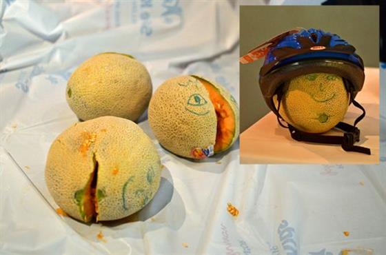 Cantaloupes with faces drawn on them with marker, one wearing a bike helmet