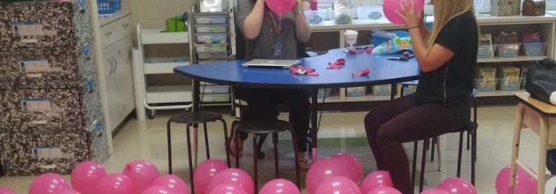 Teachers blowing up pink balloons on classroom floor