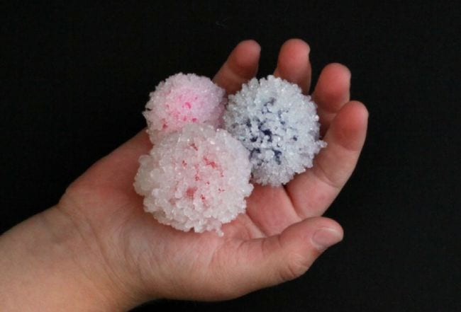 Child's hand holding crystal-covered pom pom balls (2nd Grade Science)