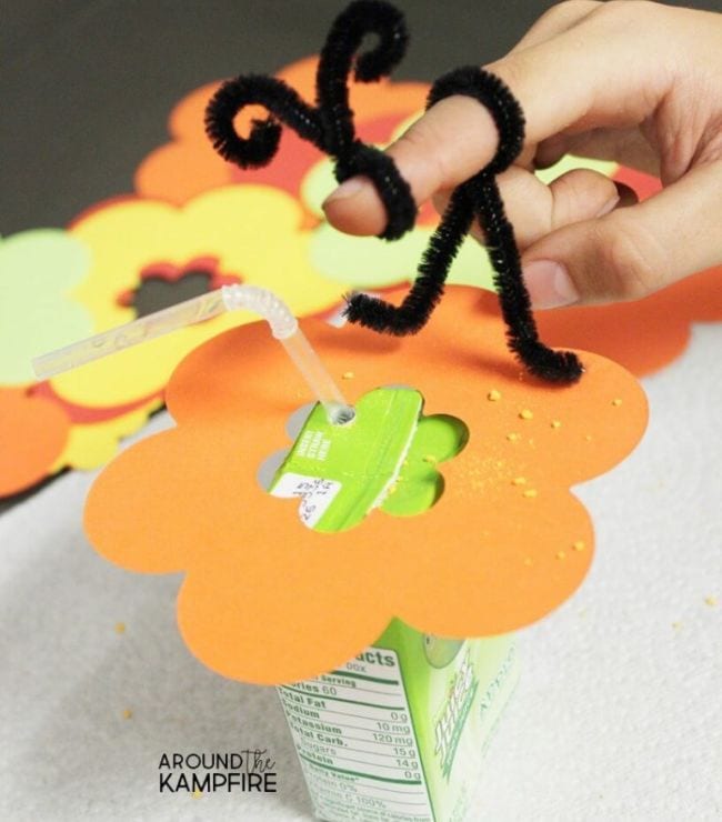 Pipe cleaner twisted into bee shape on a child's finger, sitting on a paper flower