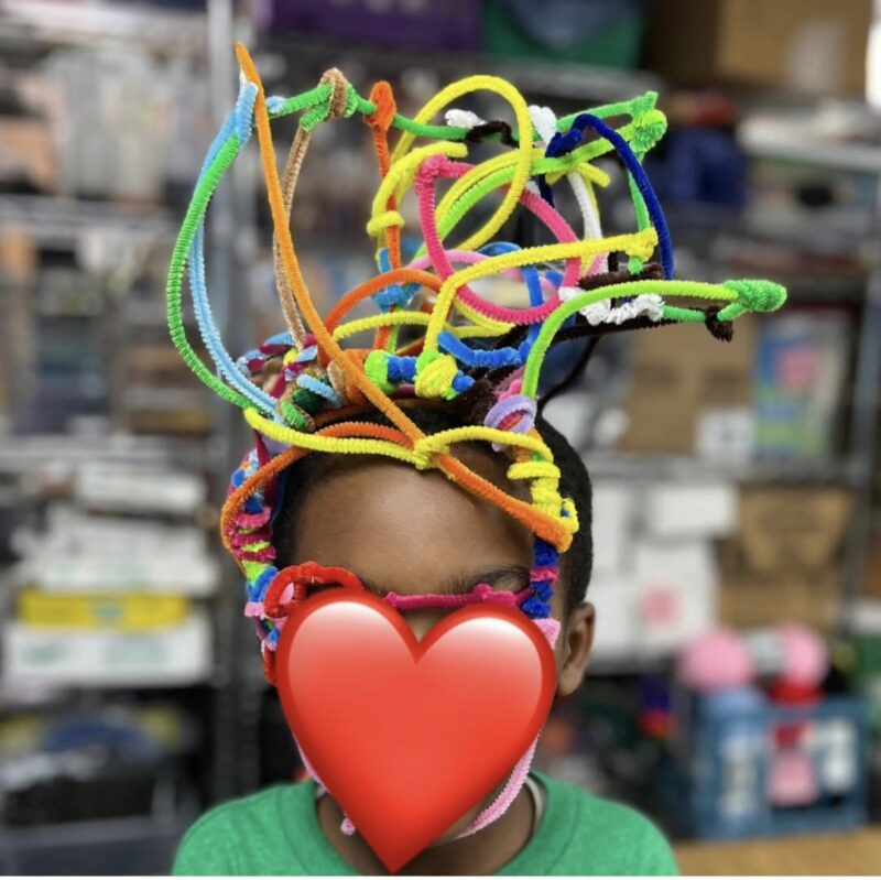 2nd grade art student wearing a hat made of pipe cleaners