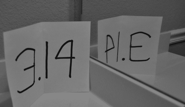 Index card with 3.14 written in black marker propped next to the mirror and showing the reflection as PIE