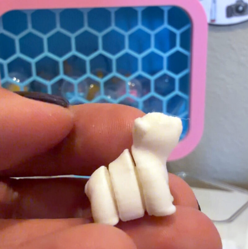 Woman's hand holding a small 3D printed bear in front of a toy capsule vending machine