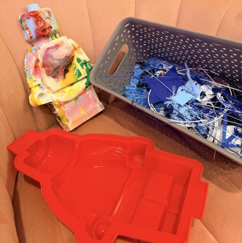 Large LEGO minifig model sitting next to a silicon mold and bin of 3D printing filament scraps
