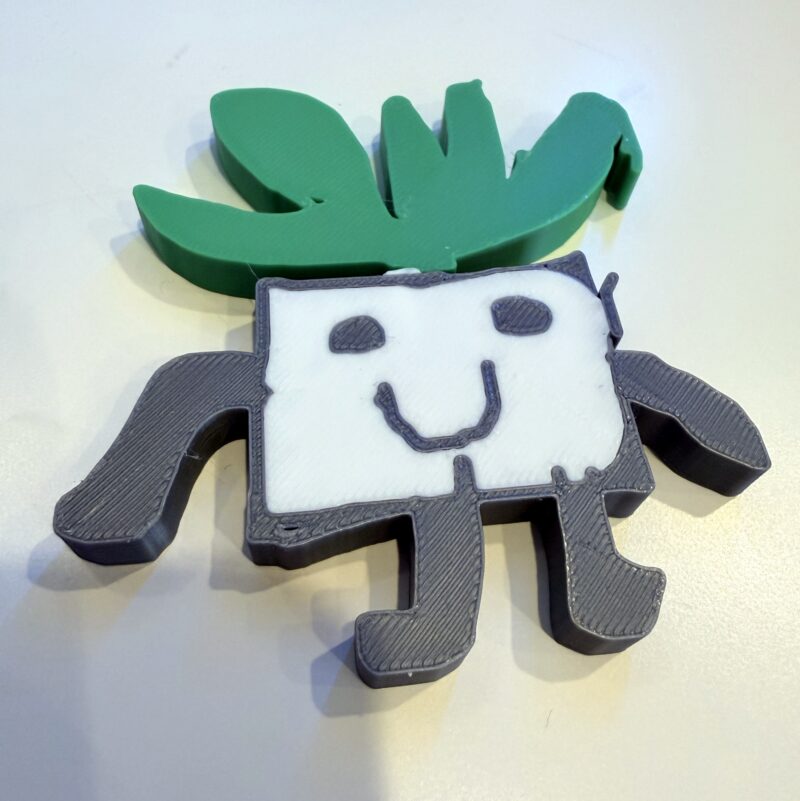 3D printed "imaginary friend" — smiling square with arms and legs and green hair on top