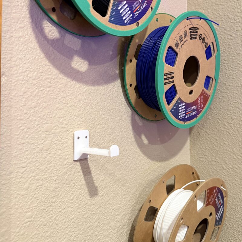 3D printing filament reels hang on the wall by a empty 3D printed wall hook