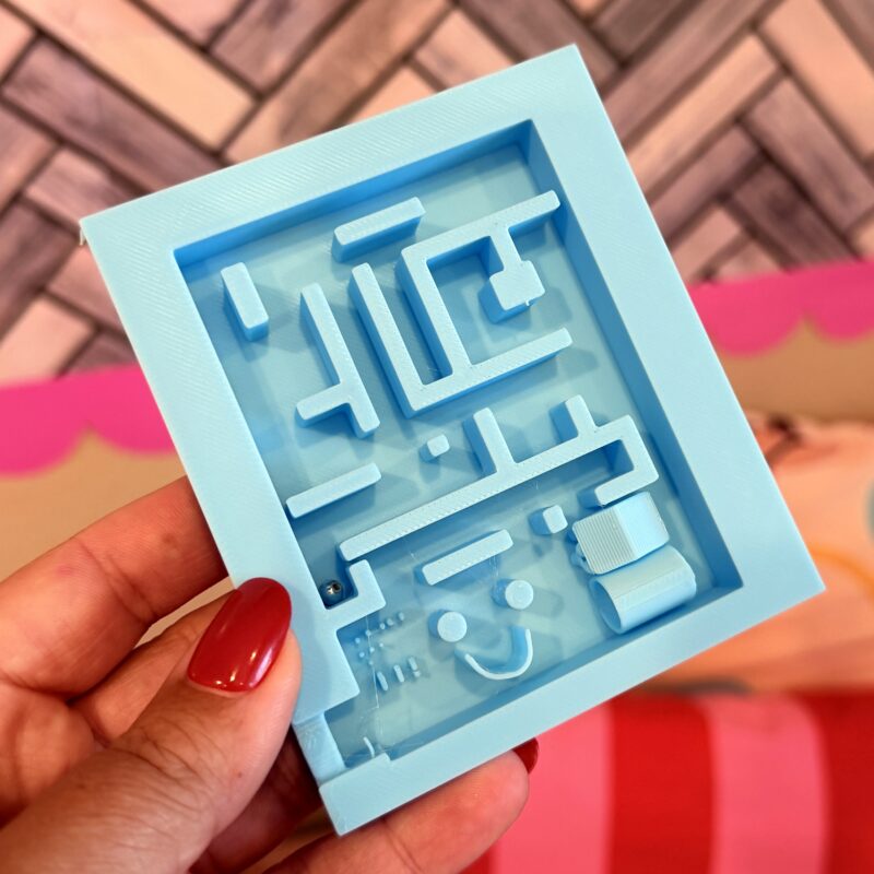 Woman's hand holding a light blue 3D printed mini marble maze 