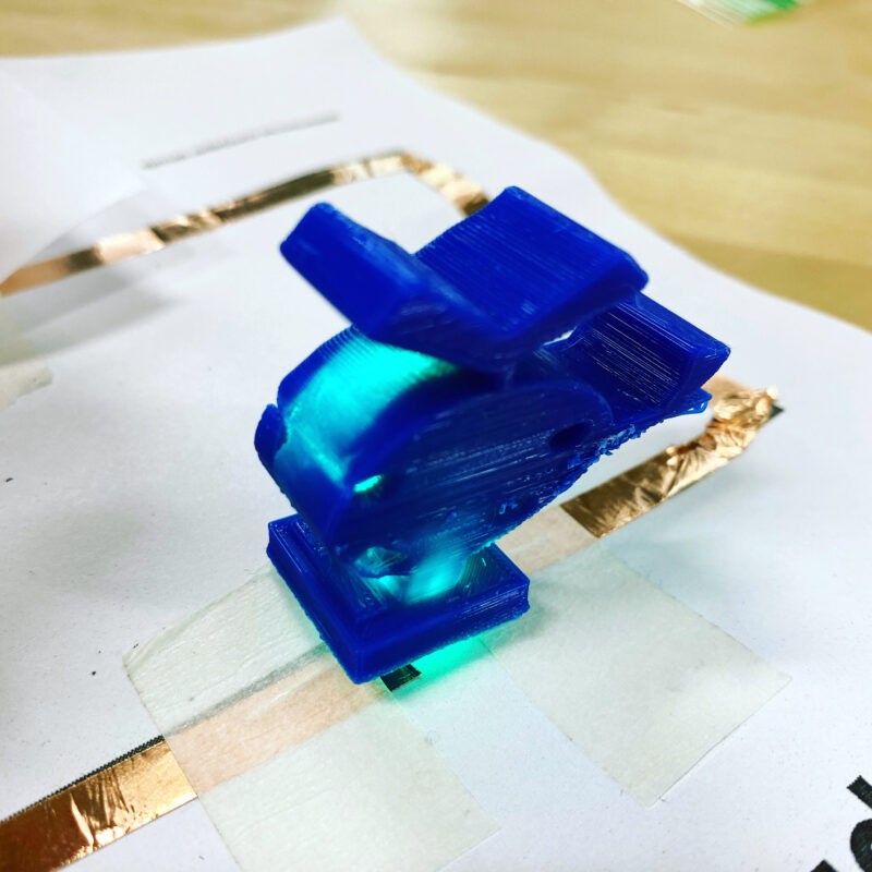 Blue 3D printed helicopter with a small light inside sitting on worksheets