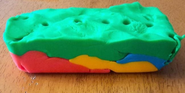 Layers of differently colored playdough with straw holes punched throughout all the layers
