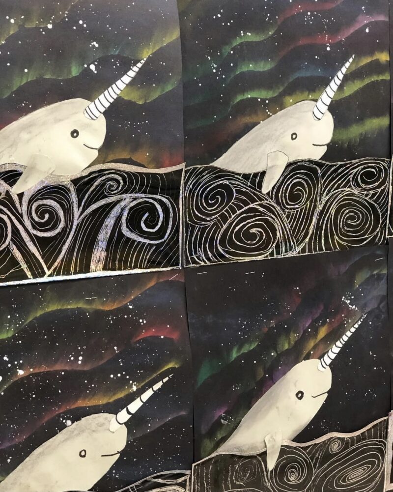 Paper narwhals on black paper with northern lights in the background