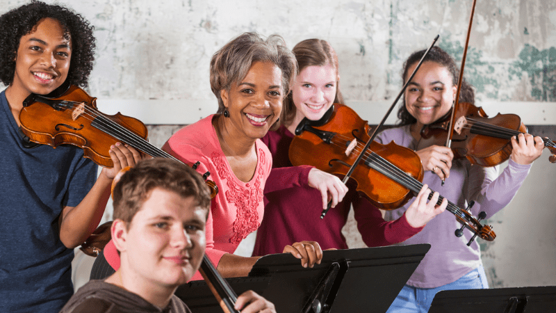 Black music education teacher teaches violin to several students