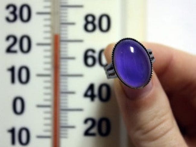 Student's hand holding a blue mood ring in front of a thermometer