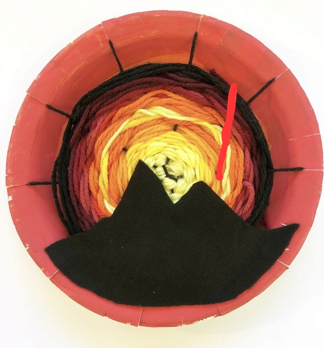 Paper plate painted orange, with red, orange, and yellow circle weaving. A paper mountain silhouette is glued on top.