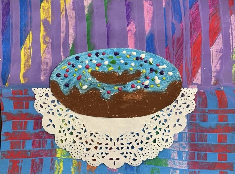 Mixed media paper donut painted with oil pastels, on a paper doily