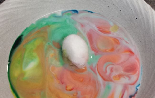 Cotton ball sitting on a bowl of milk swirled with food colors