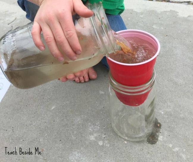 Child pouring dirty water into a cup sitting on top of a large mason jar (Fifth Grade Science)