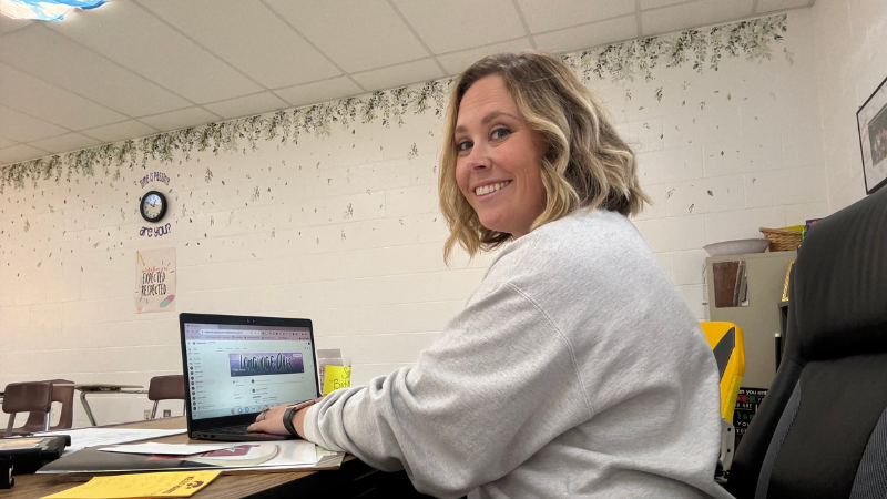 Teacher smiling at the camera as she works on a Google Chromebook