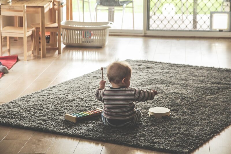 Baby sitting on rug playing with musical toys.