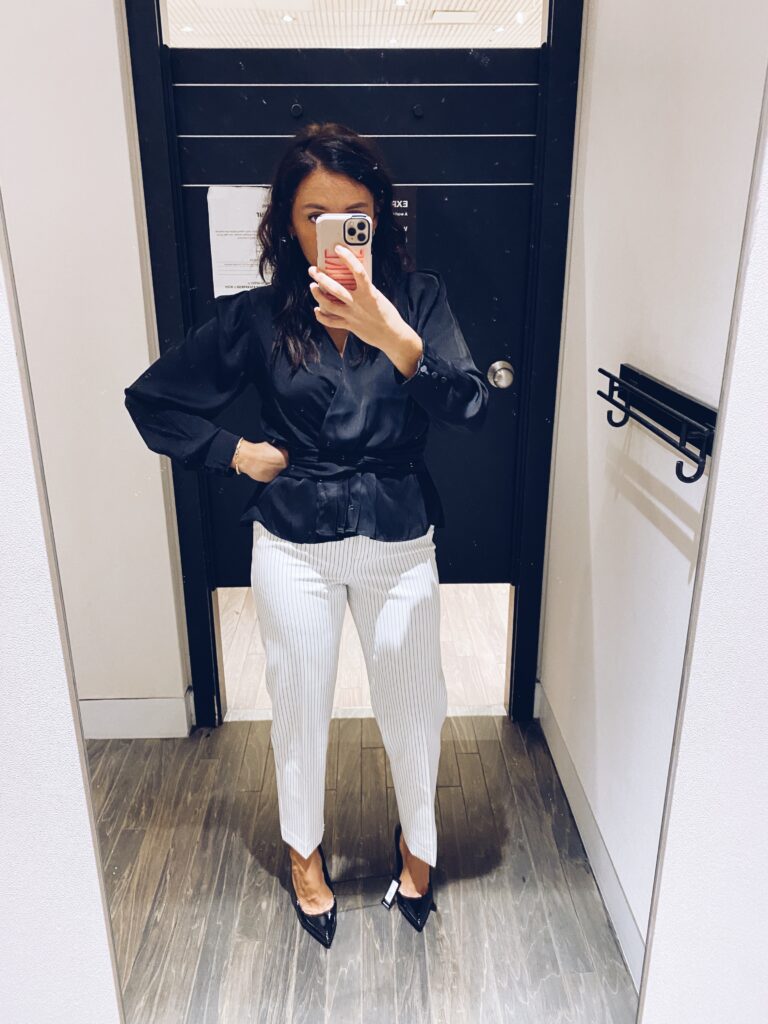 Woman posing in mirror wearing white pants and black top