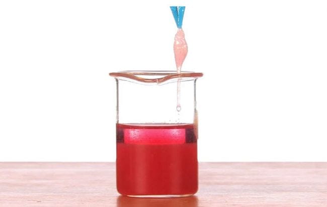Blue tweezers pulling a ball of pink goo from a beaker of red liquid (Sixth Grade Science)
