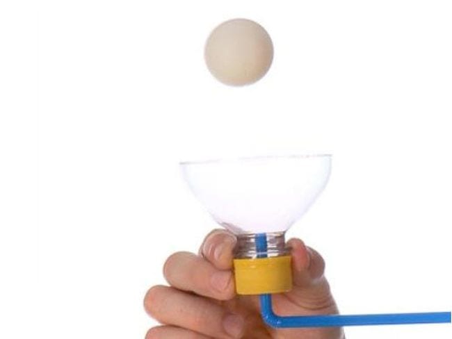 Sixth grade student holding the cut off top of a plastic bottle with a straw attached. A ping pong ball is floating over the bottle top.