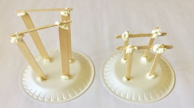 Two foam plates with structures built from wood craft sticks and putty on top