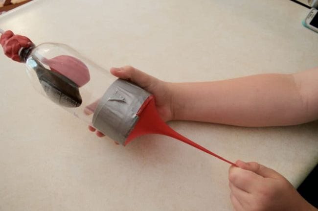 Plastic bottle with pink and black balloons inside, with student pulling a red balloon diaphragm (Easy Science Experiments)