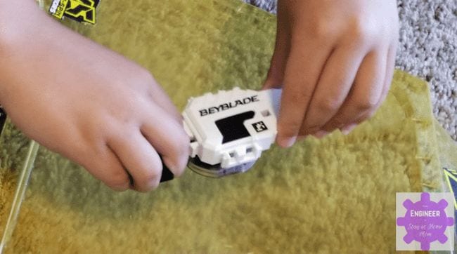 Student's hands holding a white Beyblade top (Seventh Grade Science)