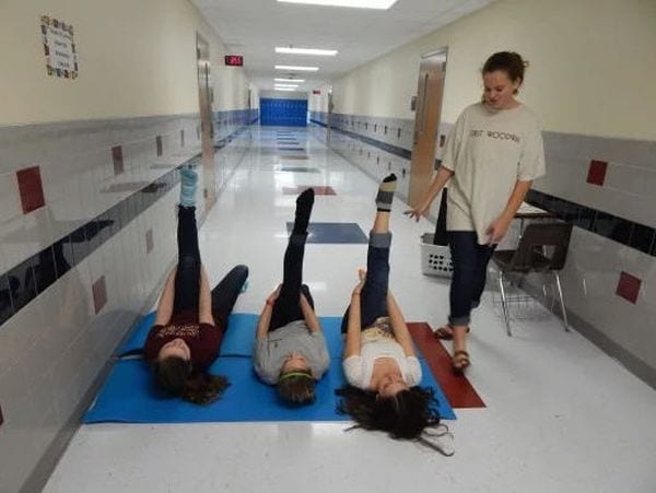 Three students lying on their backs stretching one leg in the air while another student stands nearby (Seventh Grade Science)