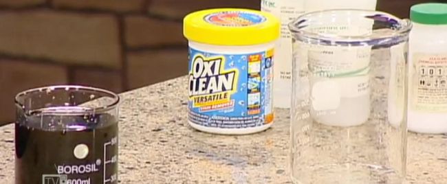 Container of OxiClean with beakers of liquid on a counter 