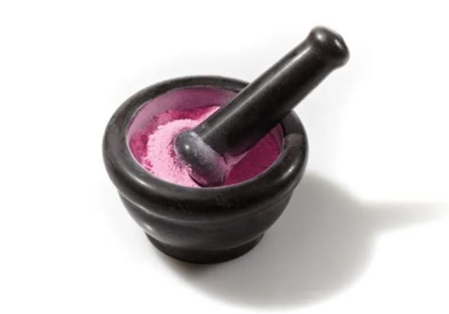 Black mortar filled with pink powder and a pestle