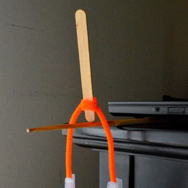 Wood craft stick balanced on end on a pencil, with orange pipe cleaner twisted around it 