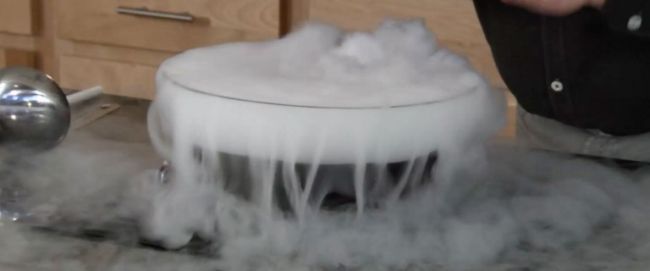 Bowl filled with root beer and dry ice, spilling over with white vapors