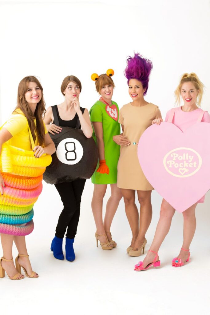 Five women are dressed as various toys from the 1990's including a magic 8 ball and a TY toy.