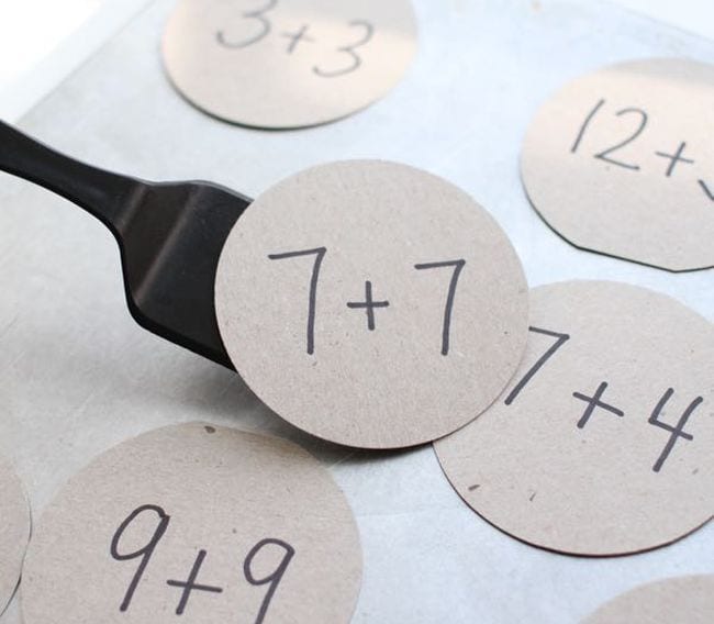 Circles of cardboard with addition problems written on them, with a spatula being used to flip one