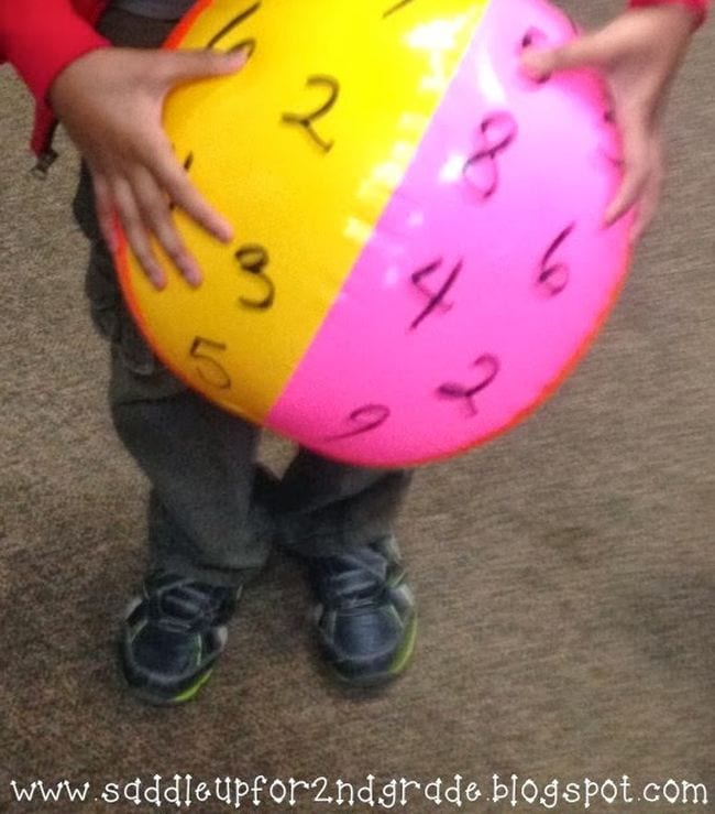Child holding a beach ball with numbers written on it in permanent marker
