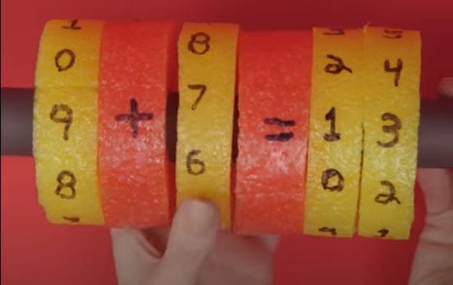 Pool noodle cut into slices and placed around a pole. Numbers and symbols are written on each slice to represent addition facts.