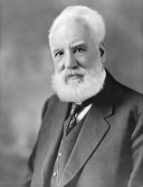 A black and white photograph of a man from the waist up is shown. He has a beard and white hair.