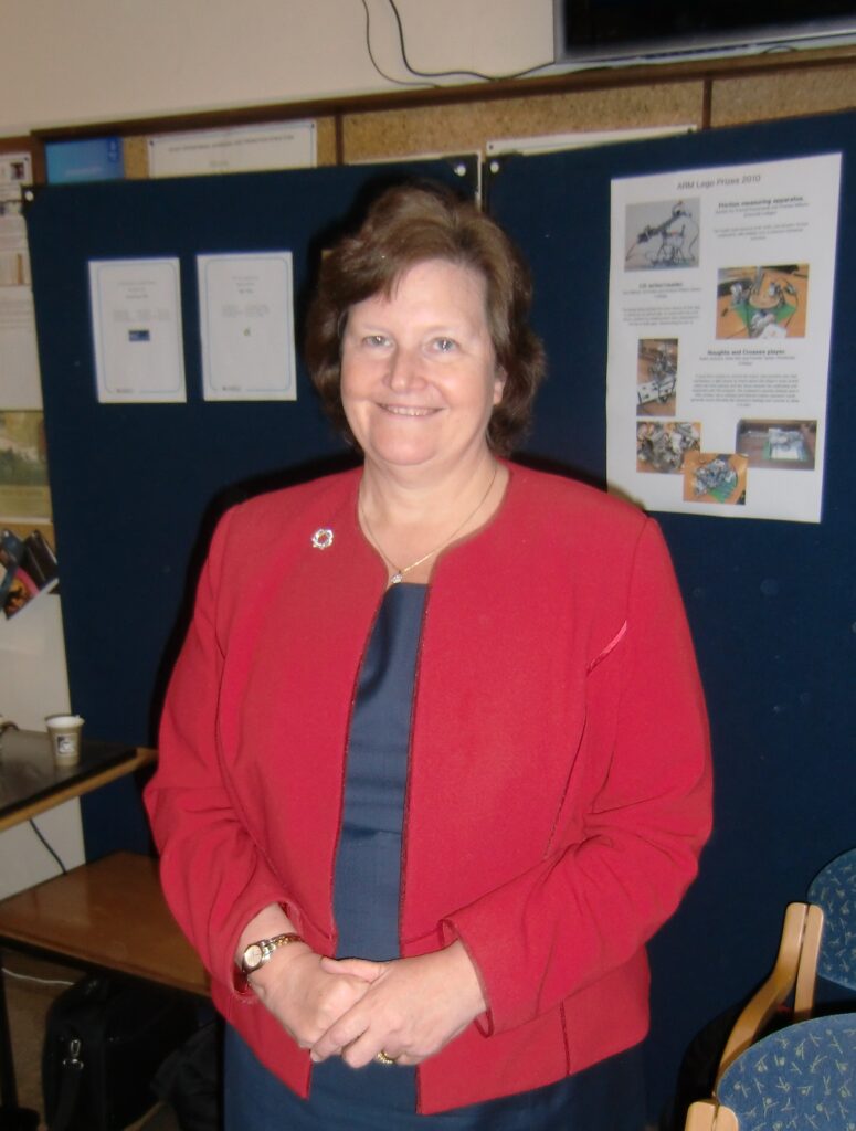 An older lady wearing a red blazer is seen from the waist up smiling.