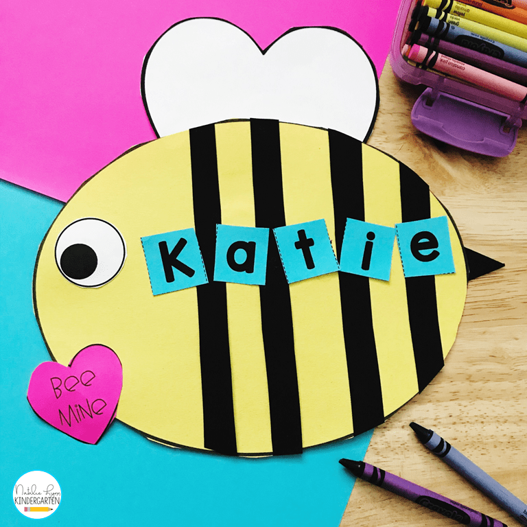 A bee is made from cardstock. It has a pink heart on it that says Bee Mine. The name Katie is spelled out across the bee's body (Valentine's Day Crafts for Preschoolers)