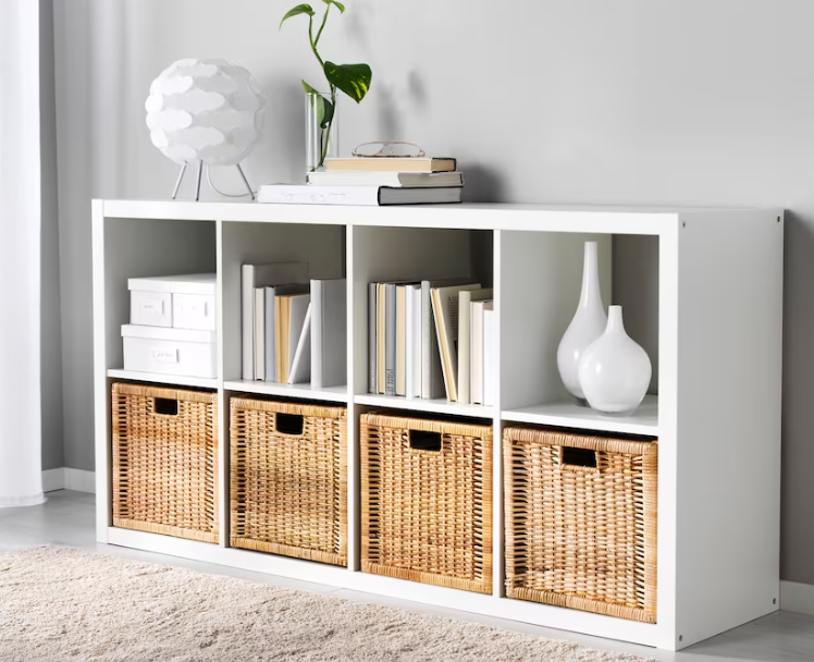 A white cubby bookshelf is shown with brown wicker baskets in the bottom shelves.