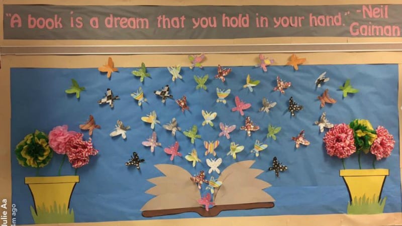 Bulletin board showing colorful butterflies emerging from an open book. Text reads "A book is a dream that you hold in your hand." -Neil Gaiman
