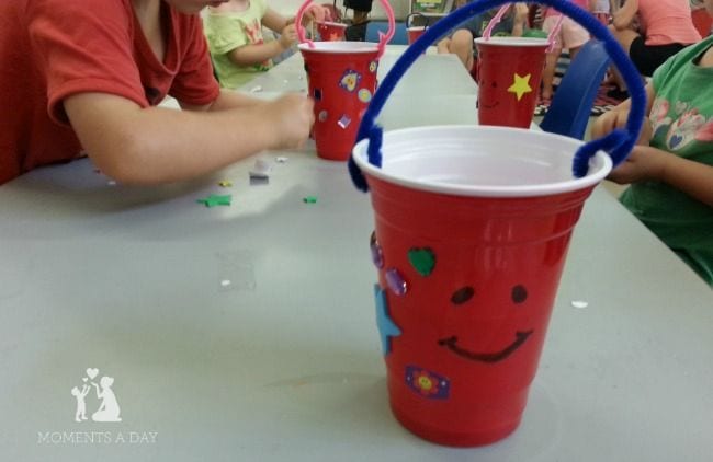 Students decorating red plastic Solo cups with stickers and a pipe cleaner handle 