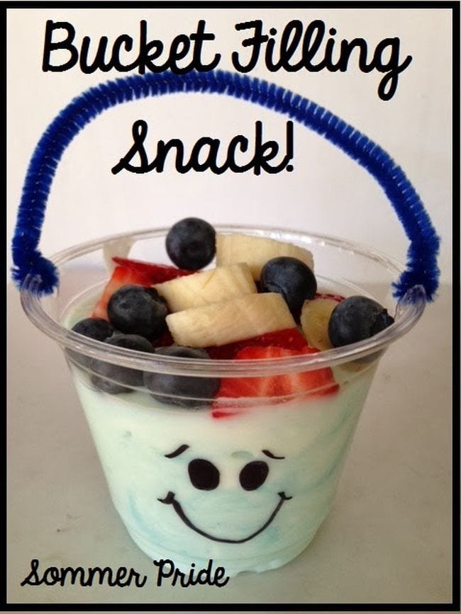 Small plastic cup of yogurt with fruit on top and a pipe cleaner handle; text reads Bucket Filling Snack!