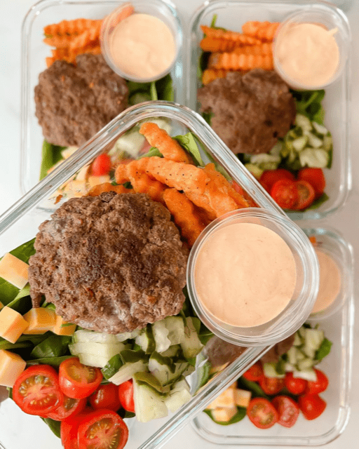 Burger with pickles and fries in a glass meal prep container